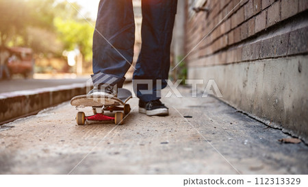 A close-up image of a male skater's feet riding on a skateboard on the street. 112313329