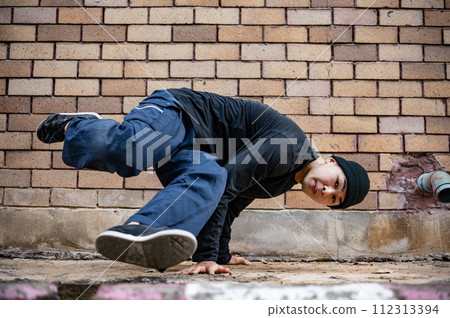 A cool Asian male hip-hop breakdancer is dancing on the street, showcasing his talented movements. 112313394