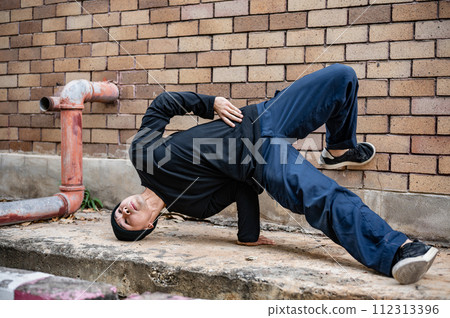 A cool Asian male hip-hop breakdancer is dancing on the street, showcasing his talented movements. 112313396