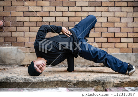 A cool Asian male hip-hop breakdancer is dancing on the street, showcasing his talented movements. 112313397