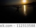 Silhouette of a man in shorts jumping into the water at a seaside pier. 112313588