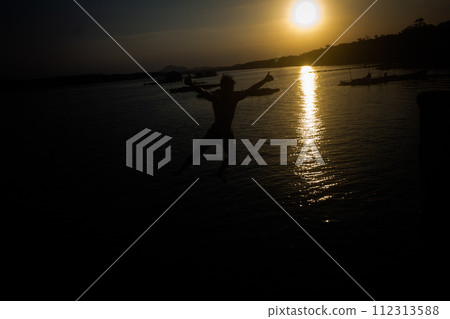 Silhouette of a man in shorts jumping into the water at a seaside pier. Silhouette of a man in shorts jumping into the water at a seaside pier. 112313588