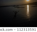 Silhouette of a man in shorts jumping into the water at a seaside pier. 112313591
