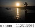 Silhouette of a man in shorts jumping into the water at a seaside pier. 112313594