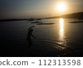 Silhouette of a man in shorts jumping into the water at a seaside pier. 112313598