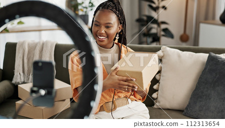 Influencer, live streaming and happy black woman with box or product in home living room. Hello, influencer and person with package, record video on social media and content creation, ring light and 112313654