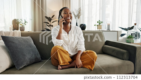 Funny, phone call and black woman on sofa, talking or communication at home. Smartphone, conversation and African person laughing, listening to story and comedy, chat or news and happy in living room 112313704