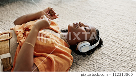 Headphones, relax and young woman on the floor in the living room listening to music or radio at modern apartment. Dancing, smile and young African female person streaming song in the lounge at home. Headphones, relax and young woman on the floor in the living room listening to music or radio at modern apartment. Dancing, smile and young African female person streaming song in the lounge at home. 112313860
