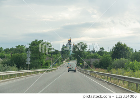 [Ukraine] Donbas region, a straight asphalt road surrounded by greenery and a church visible beyond it 112314006