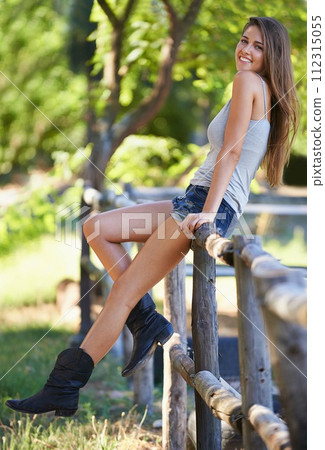 Woman, farm and portrait in outdoor, nature park and cowboy boots on holiday in summer break in sunshine. Female person, countryside and happy by fence, vacation and ranch with smile for relaxation 112315055