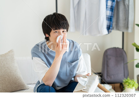 Young man blowing his nose in the living room Young man blowing his nose in the living room 112320307
