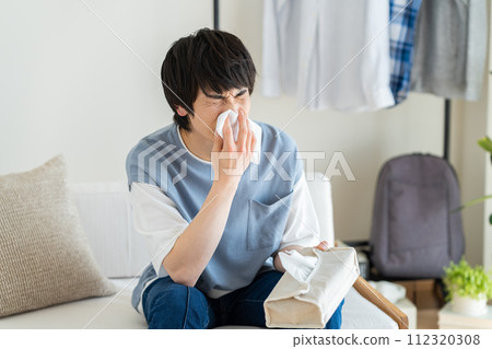 Young man blowing his nose in the living room Young man blowing his nose in the living room 112320308