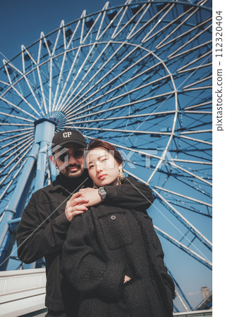 Men and women cuddling in front of the Ferris wheel 112320404