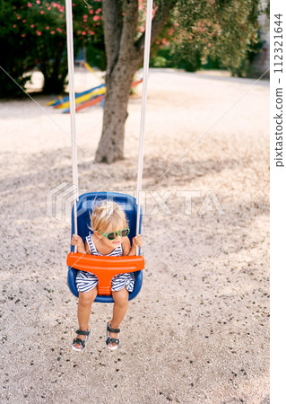 Little girl in sunglasses swinging on a swing. Top view. High quality photo Little girl in sunglasses swinging on a swing. Top view. High quality photo 112321644