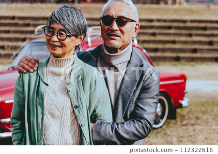 A picture of a senior couple snuggling up to the back of their car 112322618