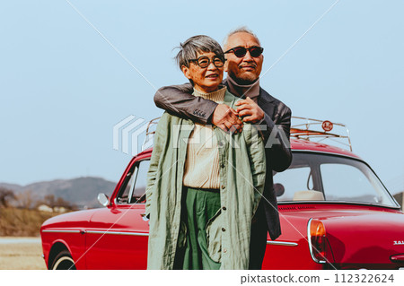A picture of a senior couple snuggling up to the back of their car A picture of a senior couple snuggling up to the back of their car 112322624