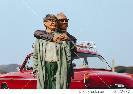 A picture of a senior couple snuggling up to the back of their car 112322627
