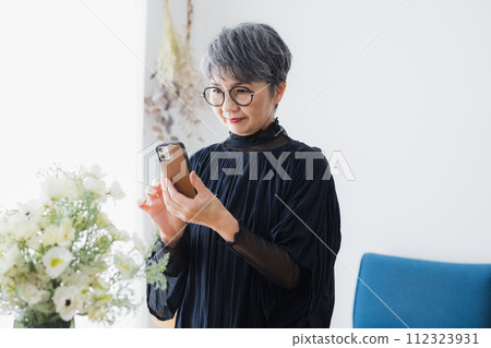 Senior woman photographing flowers in a vase 112323931