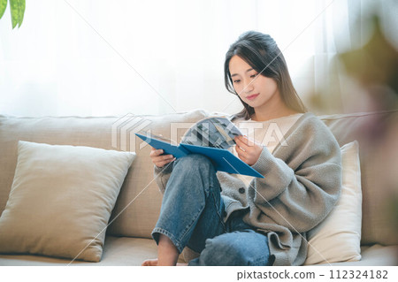 一位女士坐在被綠樹環繞的沙發上看書 112324182