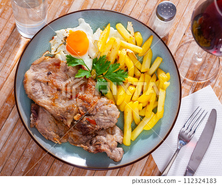 Plate of fried meat and potatoes served with fried egg decorated with parsley leaf Plate of fried meat and potatoes served with fried egg decorated with parsley leaf 112324183