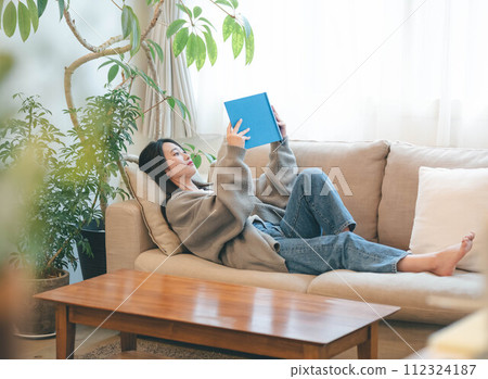 一位女士坐在被綠樹環繞的沙發上看書 一位女士坐在被綠樹環繞的沙發上看書 112324187