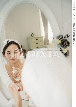 Young woman doing skin care while looking in the mirror Young woman doing skin care while looking in the mirror 112324438