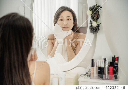 Young woman doing skin care while looking in the mirror Young woman doing skin care while looking in the mirror 112324446