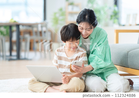 Parents and children who use a computer and a smartphone in the living room Parents and children who use a computer and a smartphone in the living room 112324886