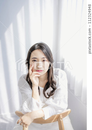 一個女人坐在靠窗的椅子上,手托著臉頰 一個女人坐在靠窗的椅子上,手托著臉頰 112324948