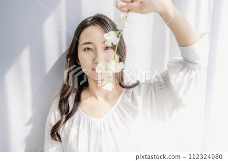 Long hair girl looking at camera holding flowers by the window Long hair girl looking at camera holding flowers by the window 112324980