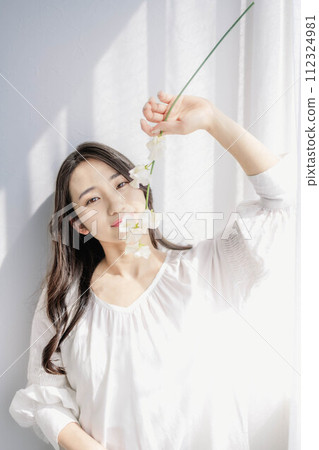 拿著花在窗邊看著相機的長發女孩 拿著花在窗邊看著相機的長發女孩 112324981