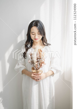 Woman with flowers standing by the window 112324990