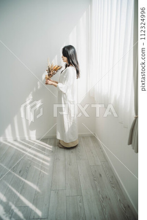 Woman with flowers standing by the window Woman with flowers standing by the window 112324996
