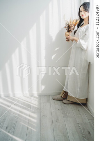 Woman with flowers standing by the window Woman with flowers standing by the window 112324997