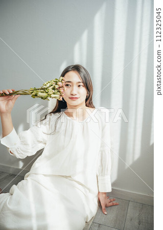 A woman in a white dress sitting on the floor by the window and holding flowers A woman in a white dress sitting on the floor by the window and holding flowers 112325045
