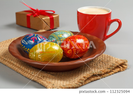 Plate with painted Easter eggs, a cup of coffee and a gift box. Plate with painted Easter eggs, a cup of coffee and a gift box. 112325094