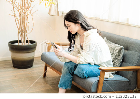 A woman operating a smartphone while relaxing on the sofa 112325132