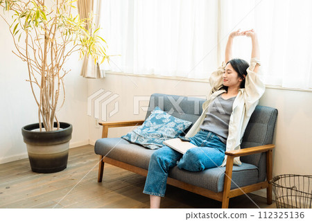 A woman taking a break and relaxing on a sofa by the window 112325136