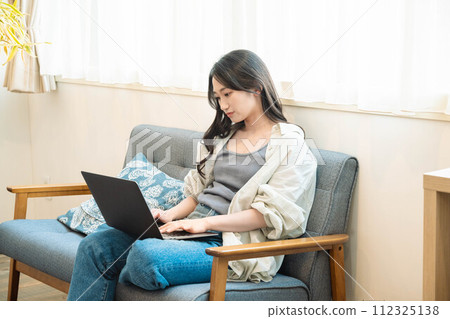 A woman sitting on a sofa and working on a computer 112325138