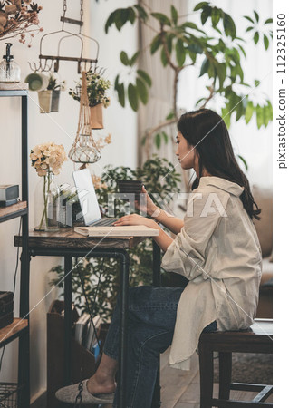 A woman working with a computer and a book in her room A woman working with a computer and a book in her room 112325160