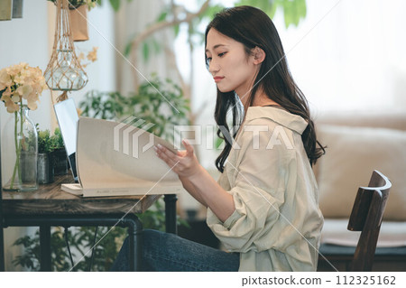 A woman working with a computer and a book in her room 112325162
