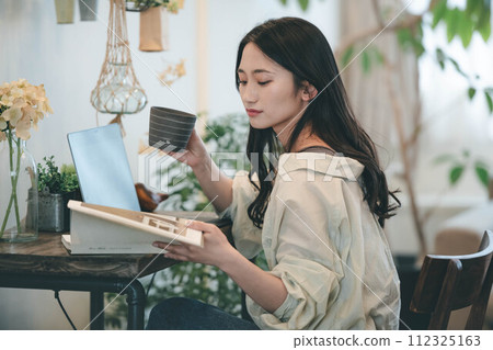 一個女人在她的房間裡用電腦和一本書工作 112325163