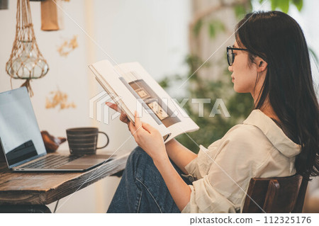 一個女人在她的房間裡用電腦和一本書工作 112325176