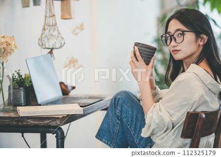 一個女人在她的房間裡用電腦和一本書工作 112325179