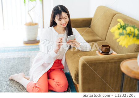 Young woman looking at her smartphone in the living room 112325203