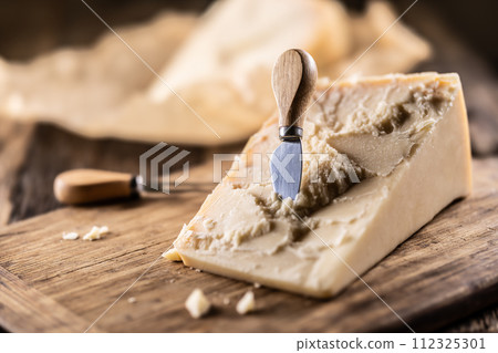 A block and pieces of Parmesan cheese on a cutting board along with a chisel and a skewer 112325301