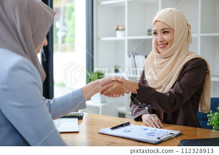 A beautiful and cheerful Asian Muslim businesswoman shaking hands with a female business partner during the meeting in the office. 112328913