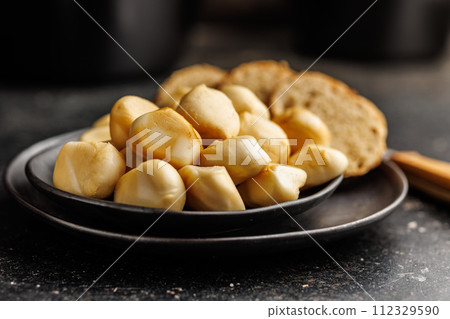 Smoked mini scamorza cheese. Traditional italian cheese on plate on black table. Smoked mini scamorza cheese. Traditional italian cheese on plate on black table. 112329590