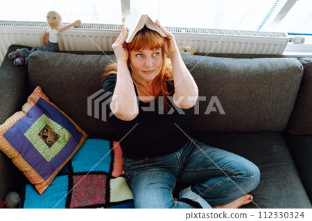 portrait middle-aged woman reading book while sitting on sofa portrait middle-aged woman reading book while sitting on sofa 112330324