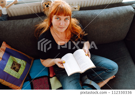 portrait middle-aged woman reading book while sitting on sofa 112330336